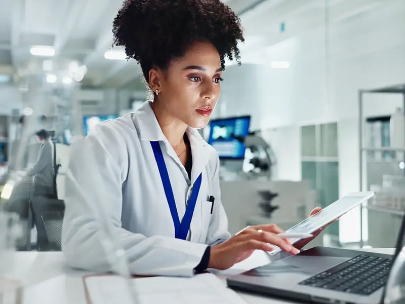 A focused scientist in a lab coat uses a digital tablet at a workstation, surrounded by modern lab equipment, conveying concentration and technology