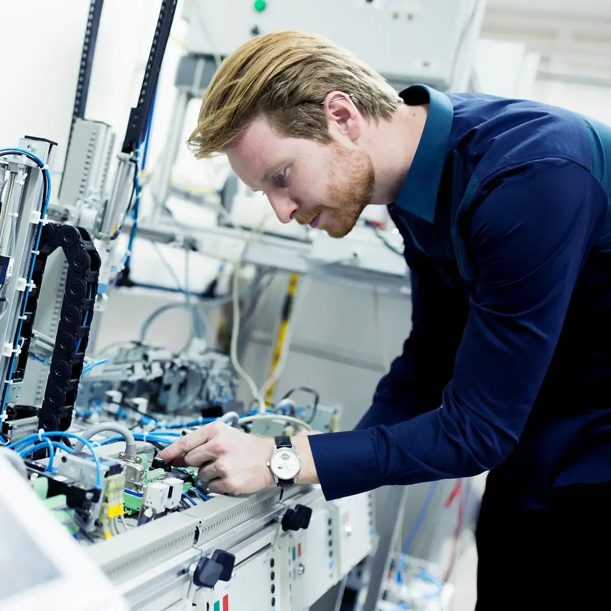 A man is focused on assembling or inspecting electronic equipment with cables in a lab setting