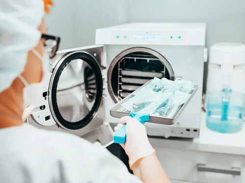 A medical professional places a tray of packaged instruments into an autoclave for sterilization