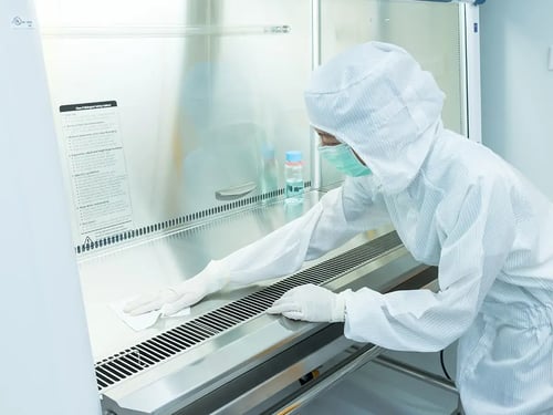 A person in full protective gear wipes down a surface inside a laboratory fume hood