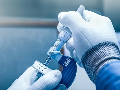 A person in white gloves uses a micrometer screw gauge, measuring with precision.