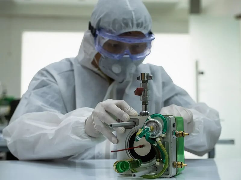 A scientist in protective gear, including a face mask and goggles, works on a complex machine with tubes in a sterile lab, conveying focus and precision
