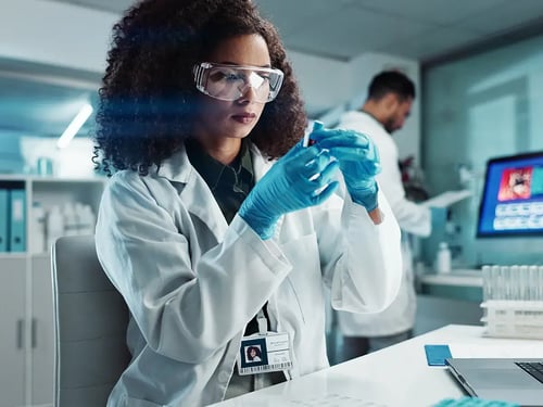 A scientist wearing a lab coat and goggles examines a test tube in a modern lab