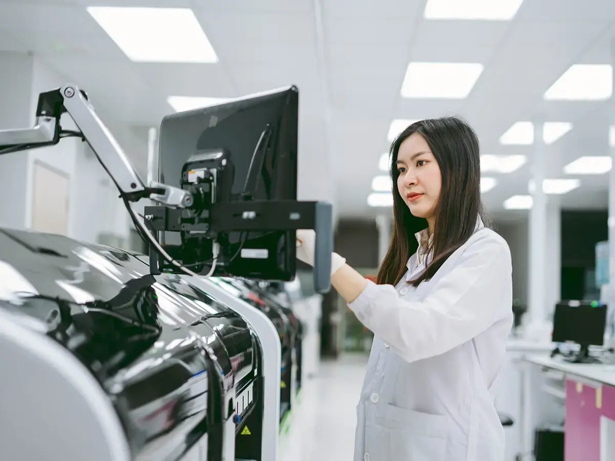 A woman in a lab coat operates a touchscreen on advanced machinery in a bright, modern laboratory