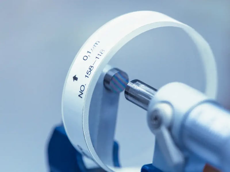Close-up of a micrometer measuring a white circular object with precise markings