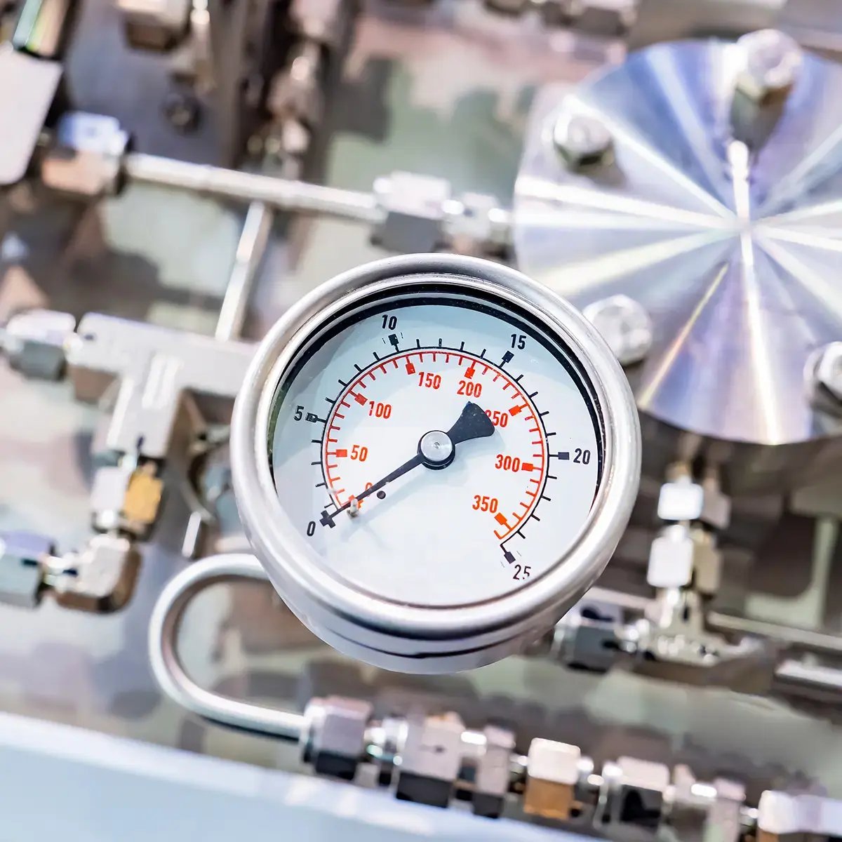 Close-up of a pressure gauge with red numbers reading up to 350 PSI, attached to a complex network of silver metal pipes and valves