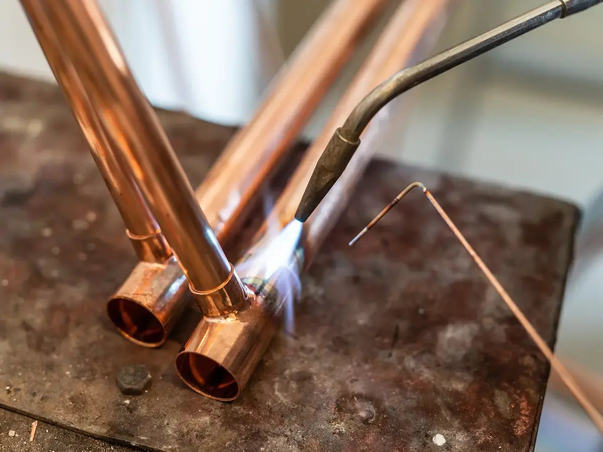 Close-up of a welding process joining copper pipes with a blowtorch, emitting a blue flame