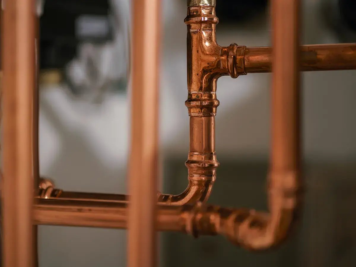 Close-up of polished copper pipes with T-joints and bends, reflecting light softly