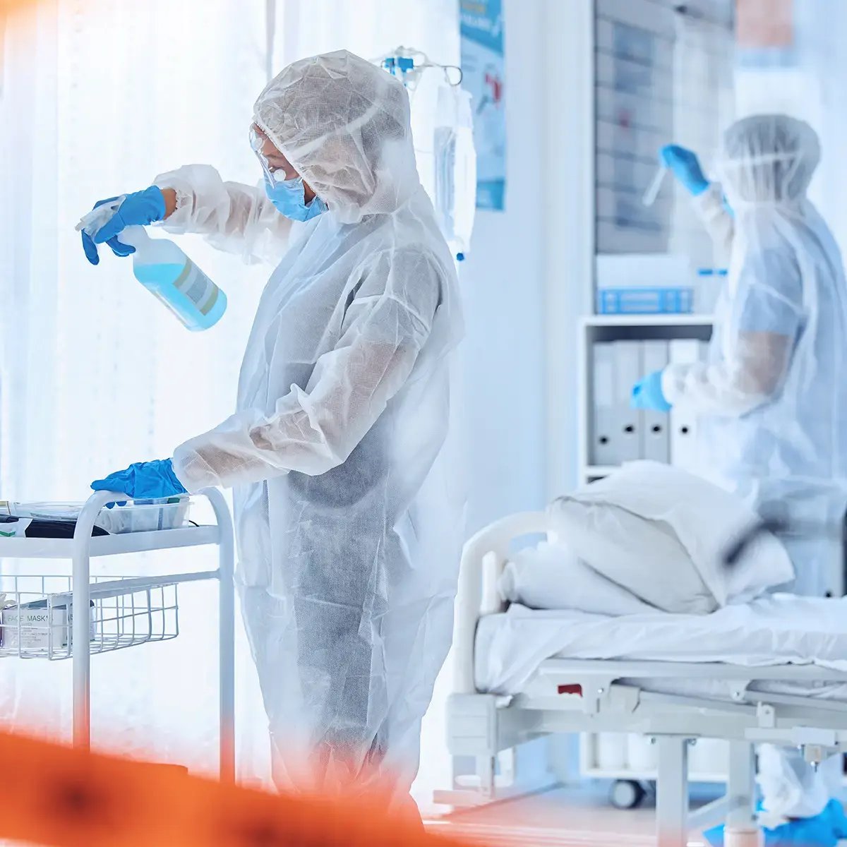 Healthcare workers in protective suits and masks clean a hospital room