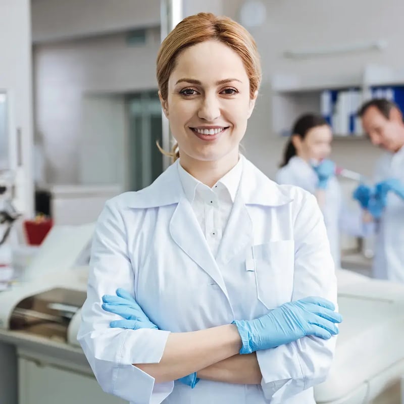 Smiling female scientist with arms crossed wearing a lab coat and gloves, standing confidently in a bright laboratory