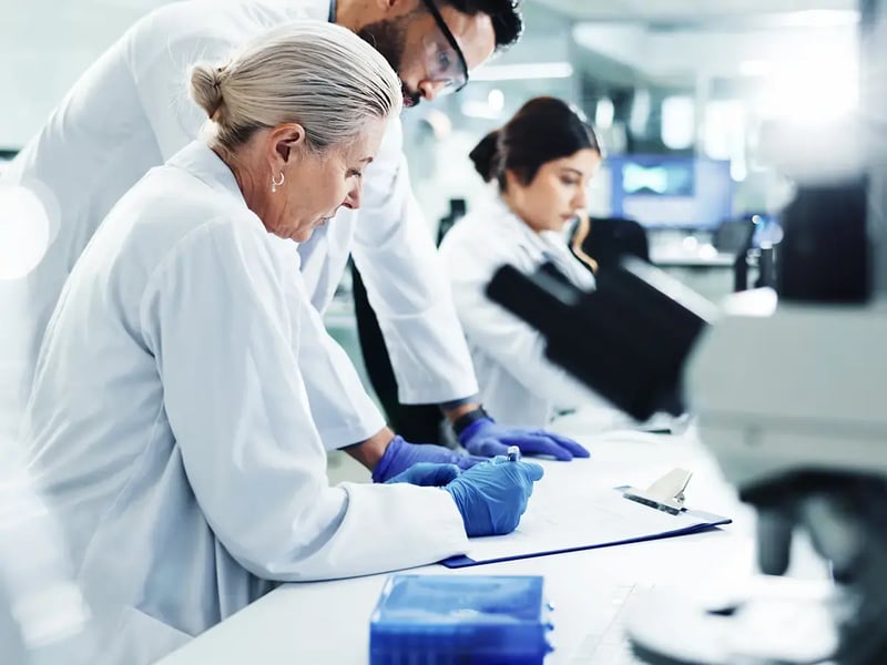 Three scientists in lab coats and gloves work attentively in a laboratory